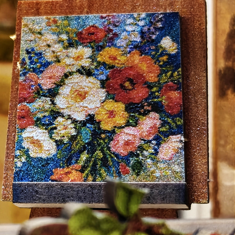 Le petit tableau floral repose sur son chevalet. Ses couleurs franches apportent un écho peint aux bouquets qui remplissent l’atelier.