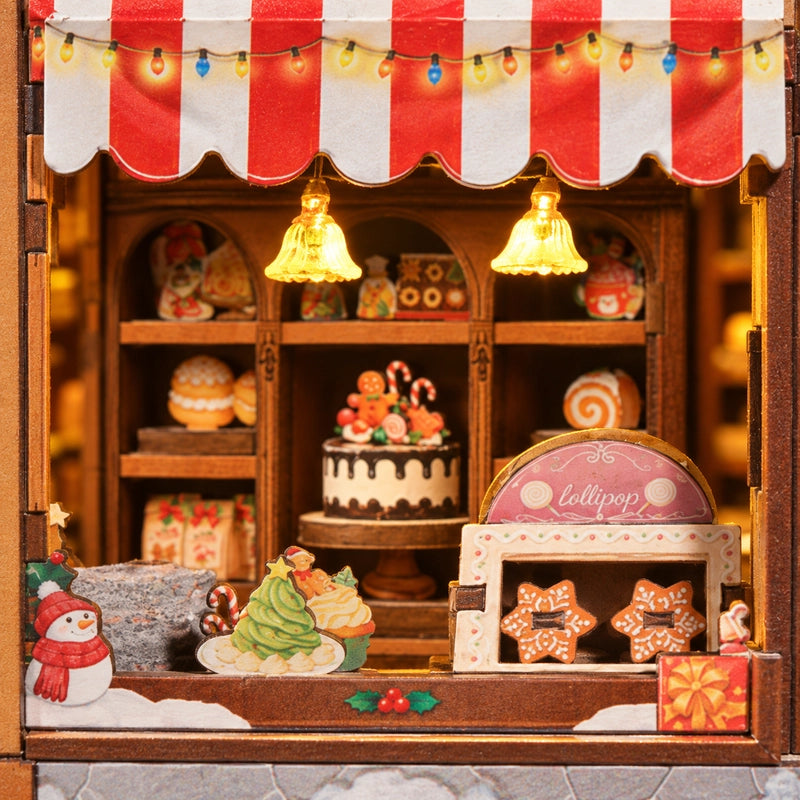 Sous deux suspensions en forme de cloche, la vitrine réunit gâteaux, petits biscuits et décorations hivernales. Le rouge, le vert et le brun s’y répondent avec chaleur.