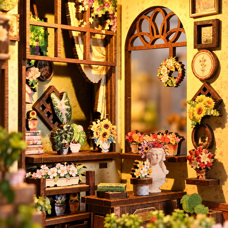 Dans l’atelier, pots fleuris, cadres botaniques et petit vase à visage se répondent autour de la fenêtre cintrée. Le décor se découvre aussi par le côté.